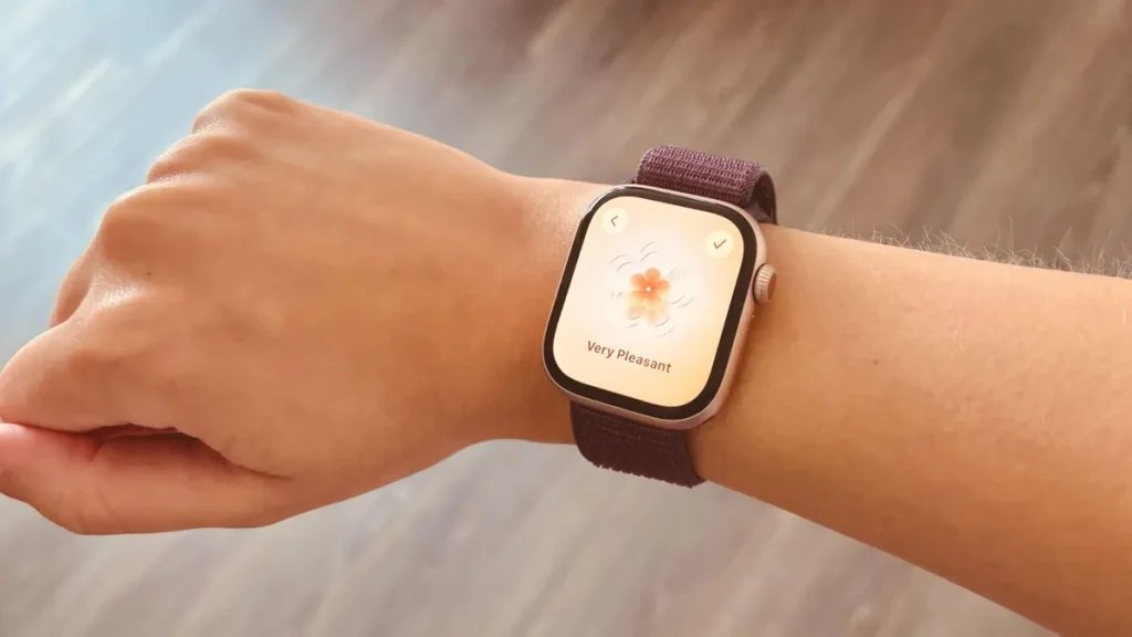 A hand with an Apple Watch 10 on it showing the State of Mind feature over a wood floor.