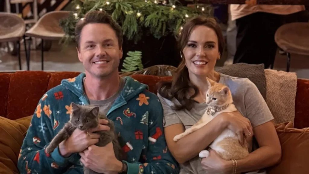 Hallmark’s 2025 ‘Countdown to Christmas’: Every New Upcoming Movie and Show A man and woman dressed in pajamas and sitting on a couch hold cats.