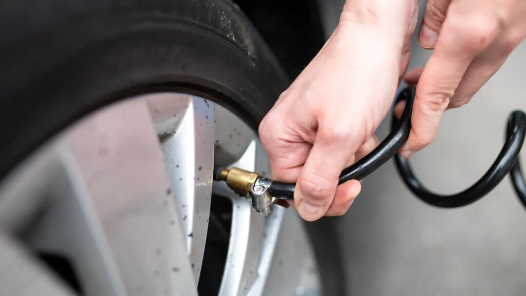 A close-up of a person's hands holding an air hose to fill a car's tire with air.