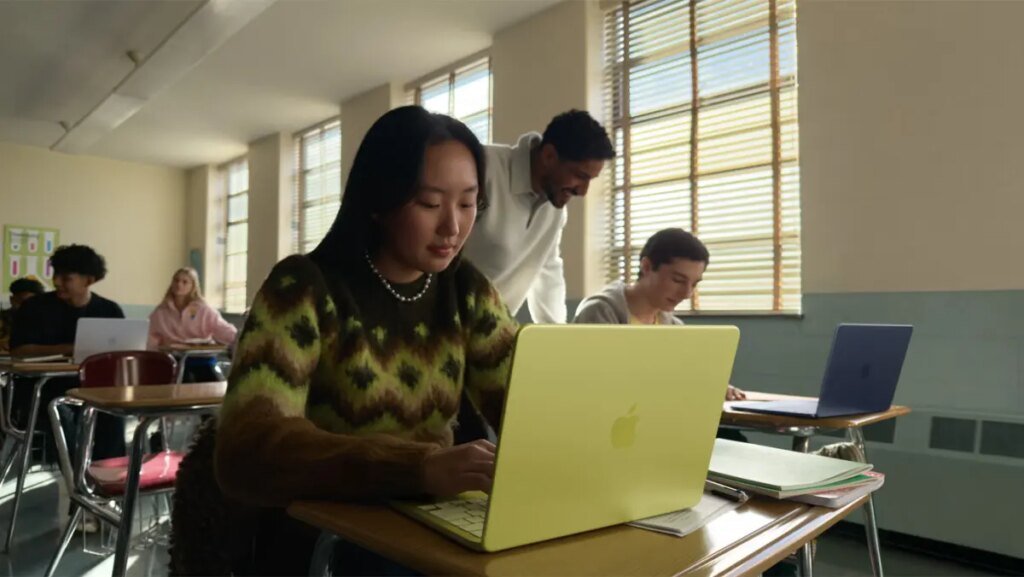 young woman seated at a classroom desk using a MacBook Neo