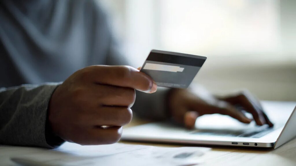 A person holds a credit card while sitting in front of a laptop computer, getting ready to make a purchase.