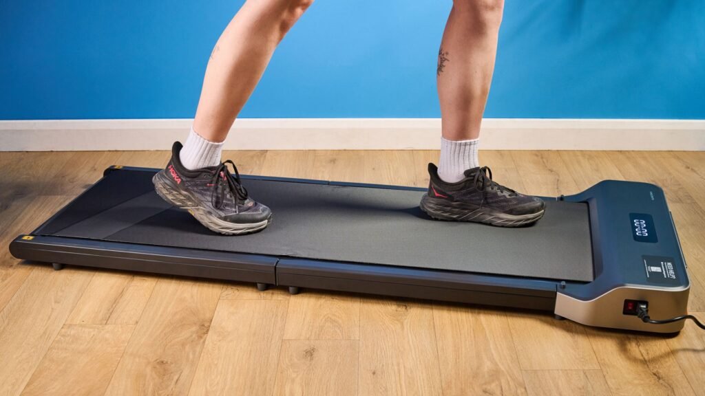 I’ve been utilizing the identical under-desk treadmill for 9 months — this is my sincere tackle all the things you want to know A woman walking on the WalkingPad Z1 wearing Hoka running shoes photographed in front of a blue background.