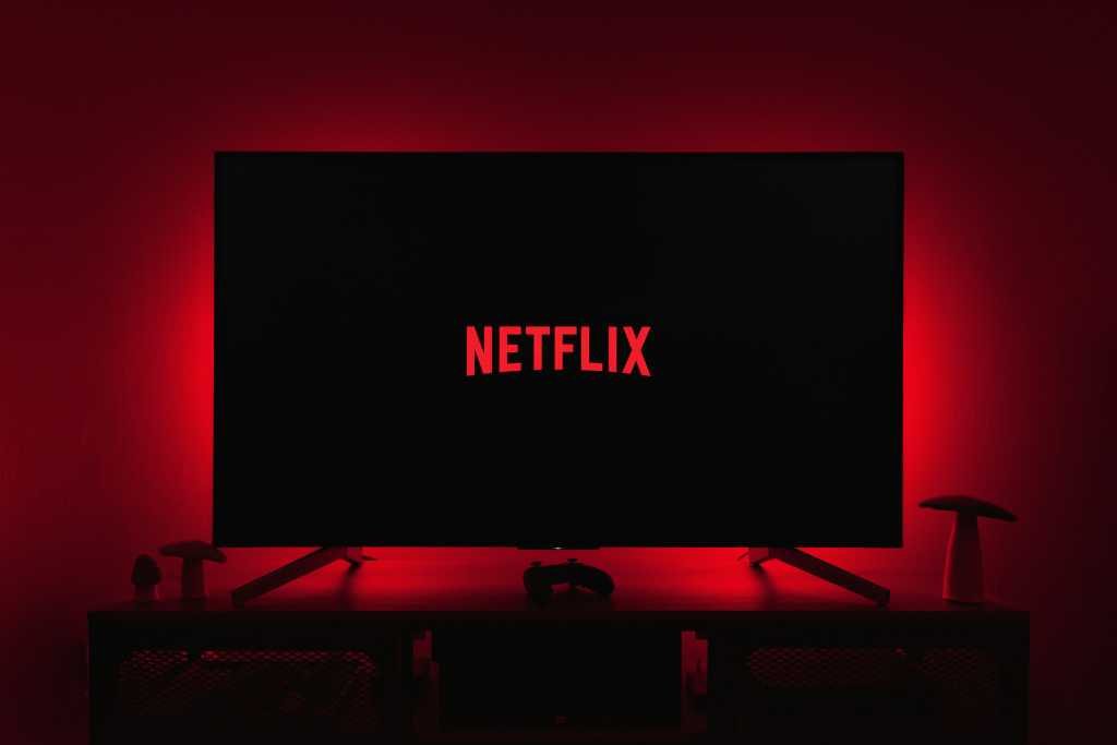 Netflix is making us pay extra, once more Netflix logo on a TV in a dark room with red backlighting