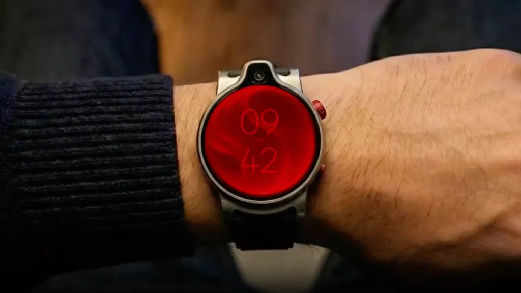 A camera-equipped prototype watch shown off by Qualcomm is being worn on a wrist. The face of the watch is red.