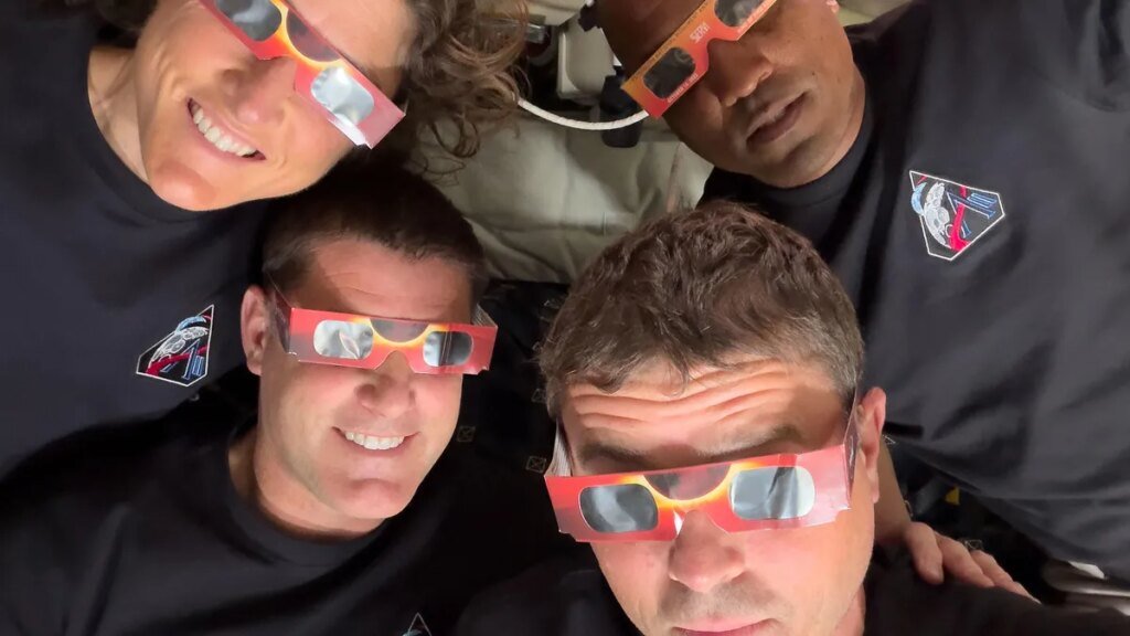 Artemis II Astronauts Are Utilizing iPhones to Seize Gorgeous House Photographs Four astronauts huddled together wearing eclipse glasses.