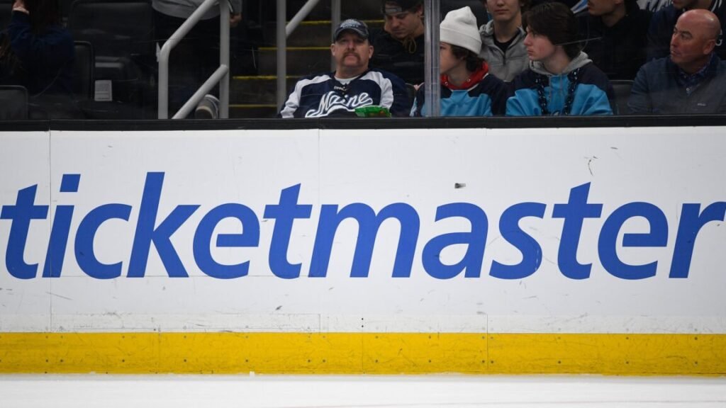 A large Ticketmaster logo on the boards inside an ice hockey arena.