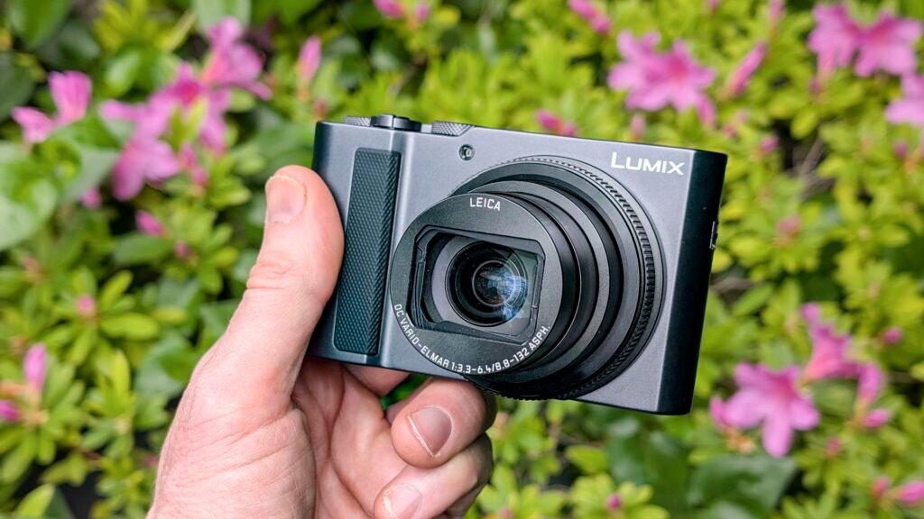 Panasonic Lumix TZ300 compact camera in the hand with a colorful floral backdrop