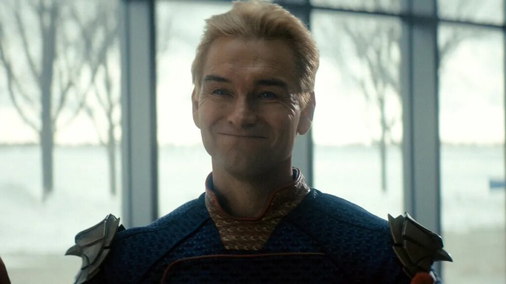 A production still from The Boys showing blonde Antony Starr closed mouth smiling in a superhero costume.