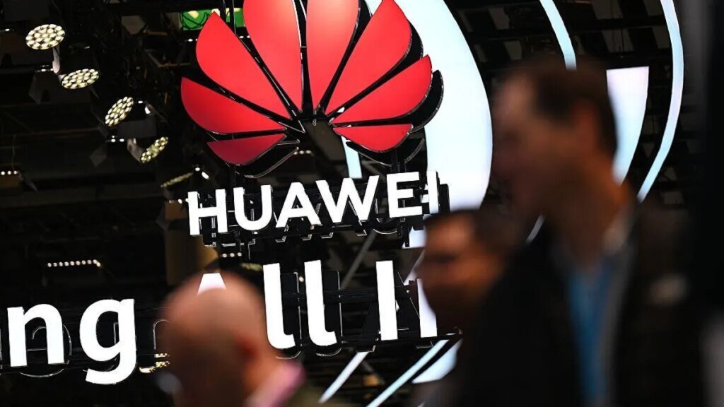 Trump Administration Bans Chinese language Routers. Telephones and Cameras Might Observe Huawei's logo hangs from the ceiling as several blurry people pass by the camera in the foreground.