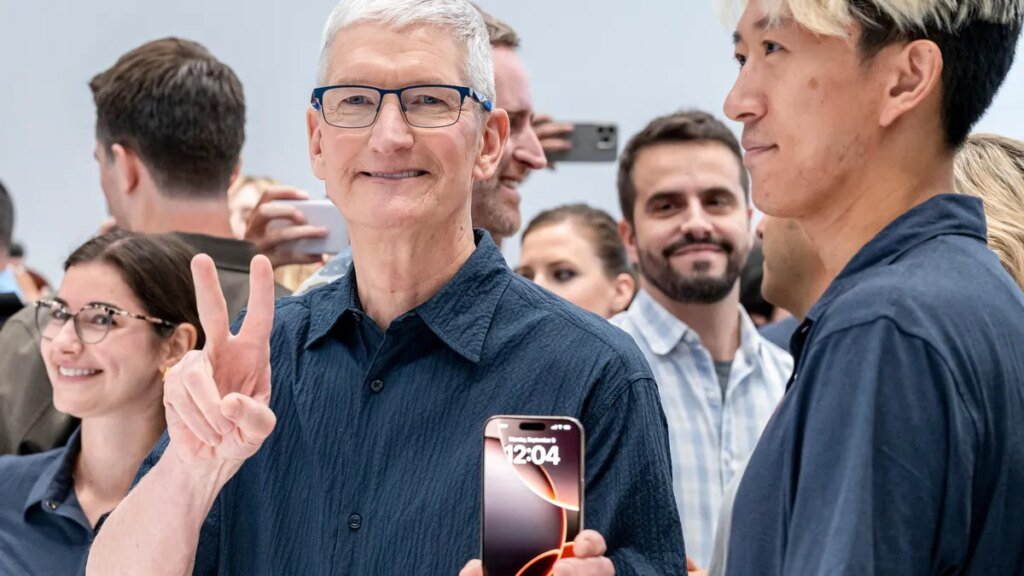 A smiling man flashes a peace sign with one hand while holding an iPhone in the other.