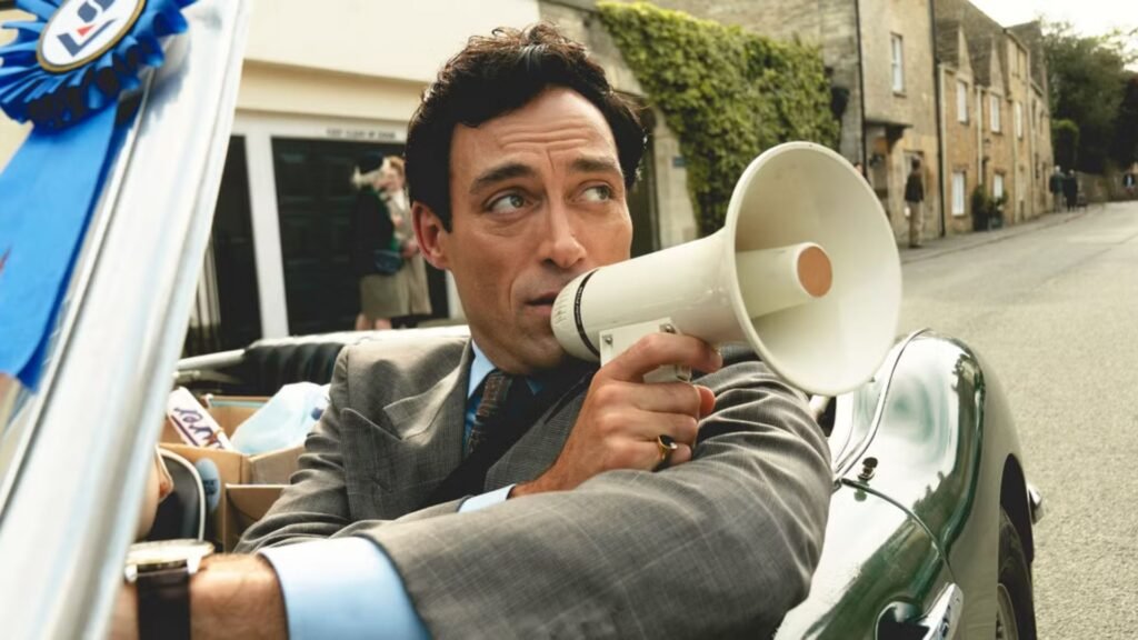 Rupert Campbell-Black talks through a megaphone while driving a convertible