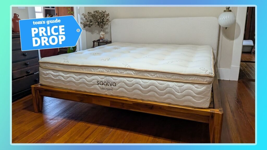 The Saatva Latex Hybrid Mattress on a bed frame in our tester's bedroom. A Tom's Guide Price Drop deals graphic in the top left corner